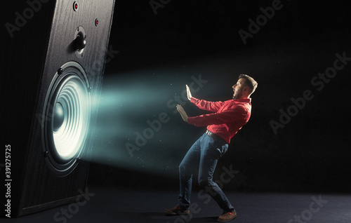 The sound wave from big sound speaker set back a screaming man in red shirt on black background. Image.