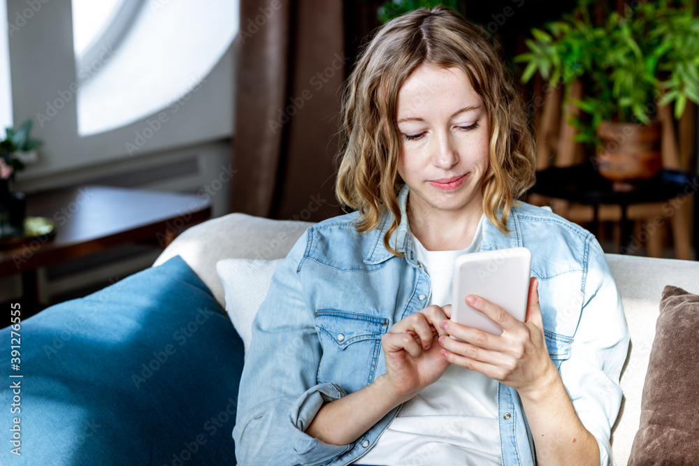 Blond woman using mobile phone for online shopping sitting in a couch at home Blond woman using mobile phone for online shopping sitting in a couch at home
