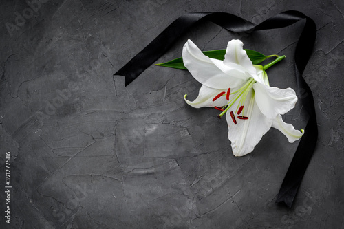 Flat lay of lily flowers and black ribbon. Funeral symbol photo