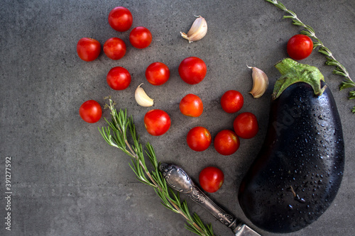 Fresh vegetables on grey background with copy space. Cooking ingredients on a table. Eggplant, cherry tomatoes and rosemary top view photo. 