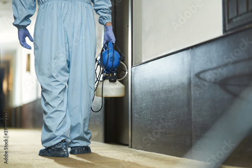 Man in a special protective suit using disinfectant in hotel