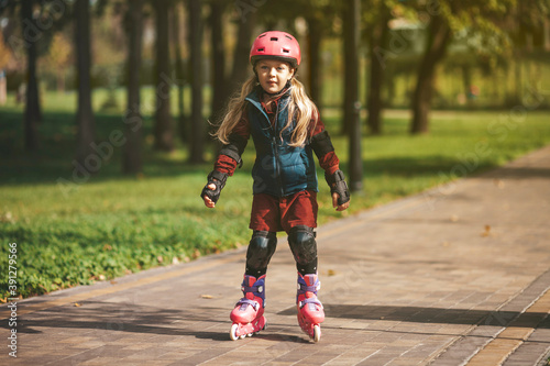 Cute preschooler girl is rollerblading in the park.