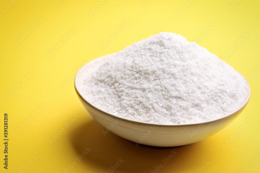 Bowl with salt on yellow background, closeup