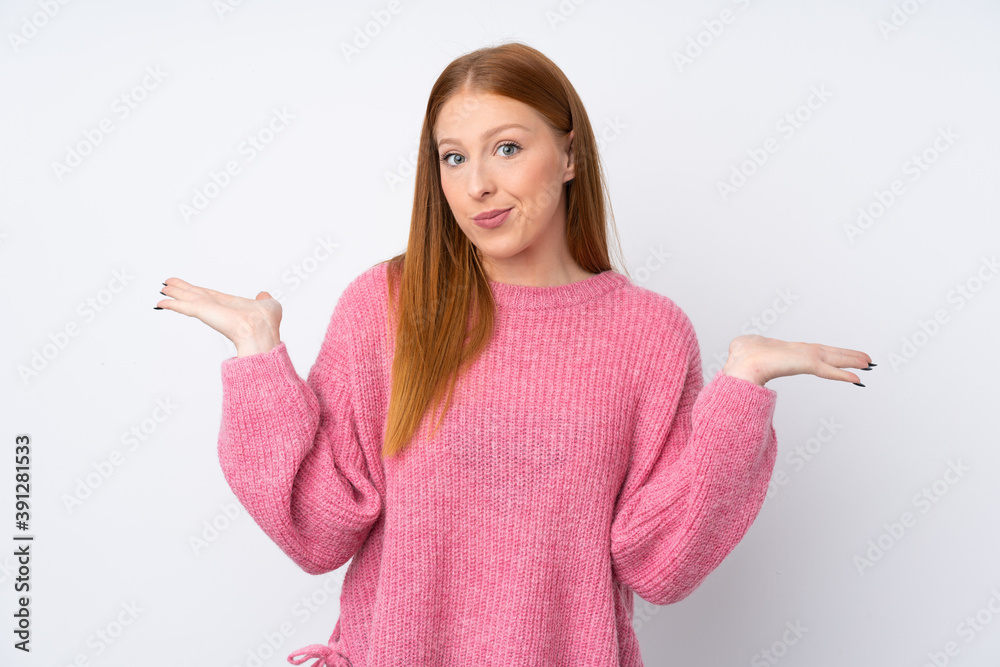 Young redhead woman with pink sweater over isolated white background having doubts while raising hands Young redhead woman with pink sweater over isolated white background having doubts while raising hands