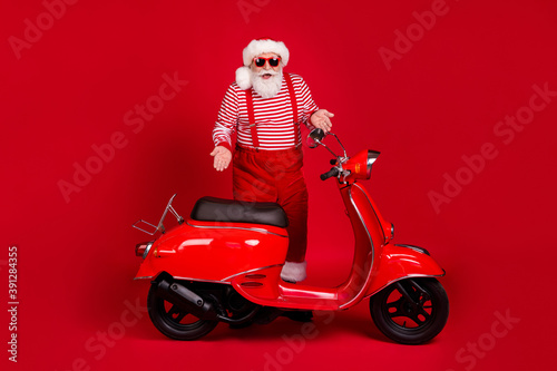 Full length body size view of his he handsome cheerful cheery glad bearded Santa father learn riding moped gift present surprise sale discount isolated bright vivid shine vibrant red color background