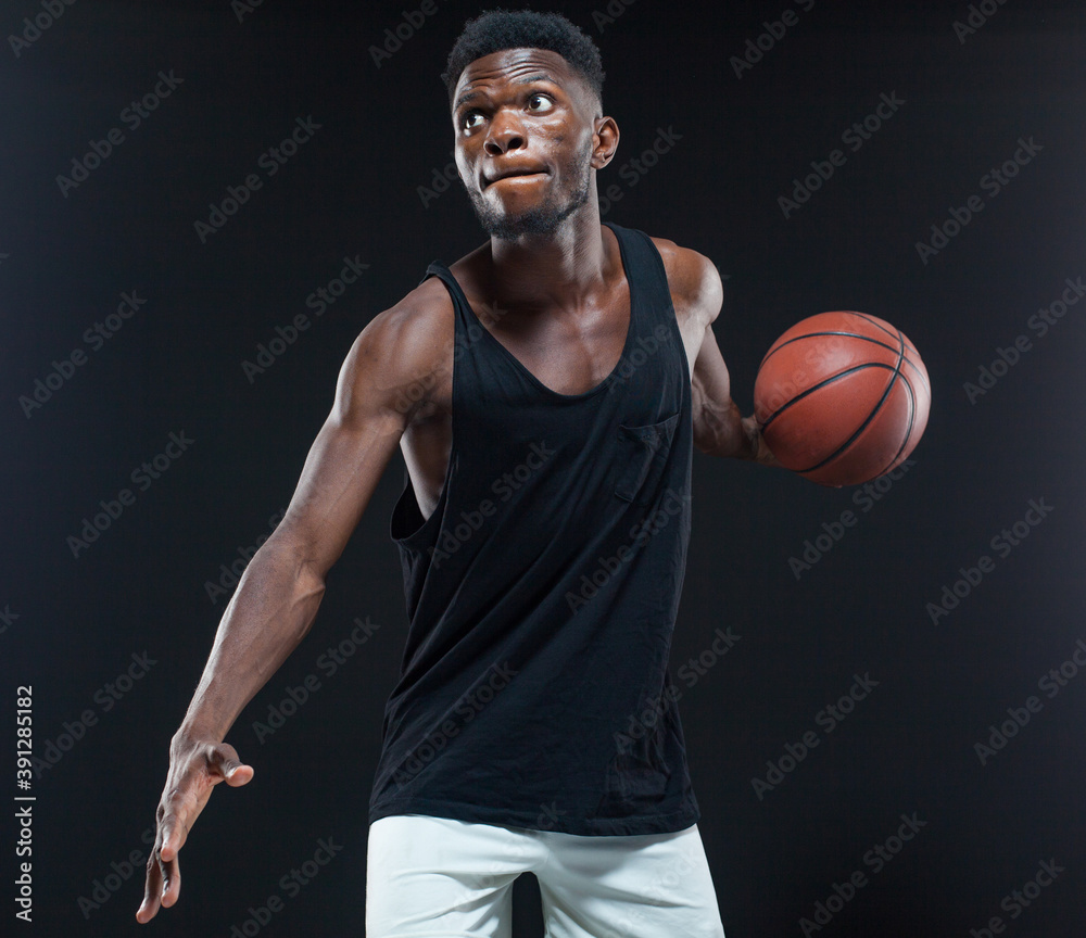 Portrait of afro american male basketball player playing with a ball over black background. Fit young man in sportswear holding basketball Portrait of afro american male basketball player playing with a ball over black background. Fit young man in sportswear holding basketball
