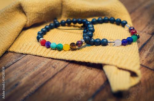two stone bracelets for healing crystal therapy, with lava stones and different crystals on a wooden table and yellow cloth
