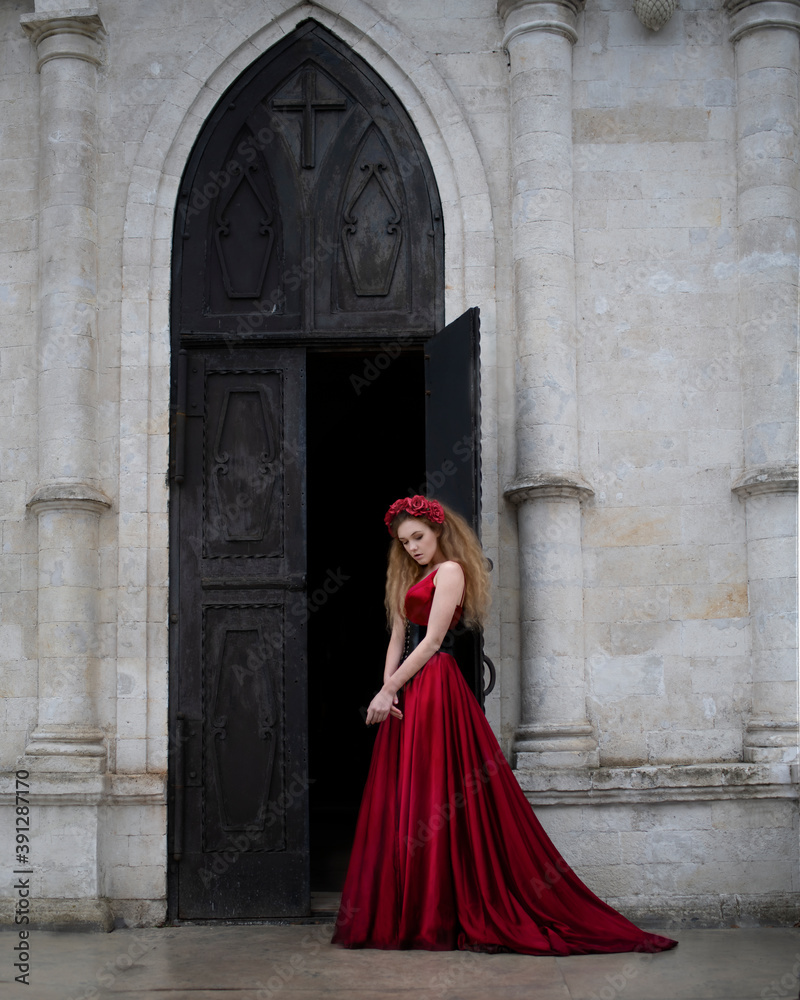 Art photo of a woman in a red dress at the door of a gothic temple