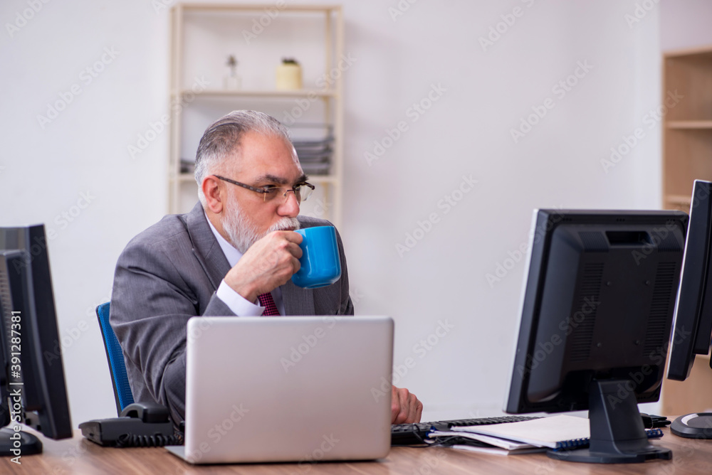 Old male boss sitting at desktop in the office Old male boss sitting at desktop in the office