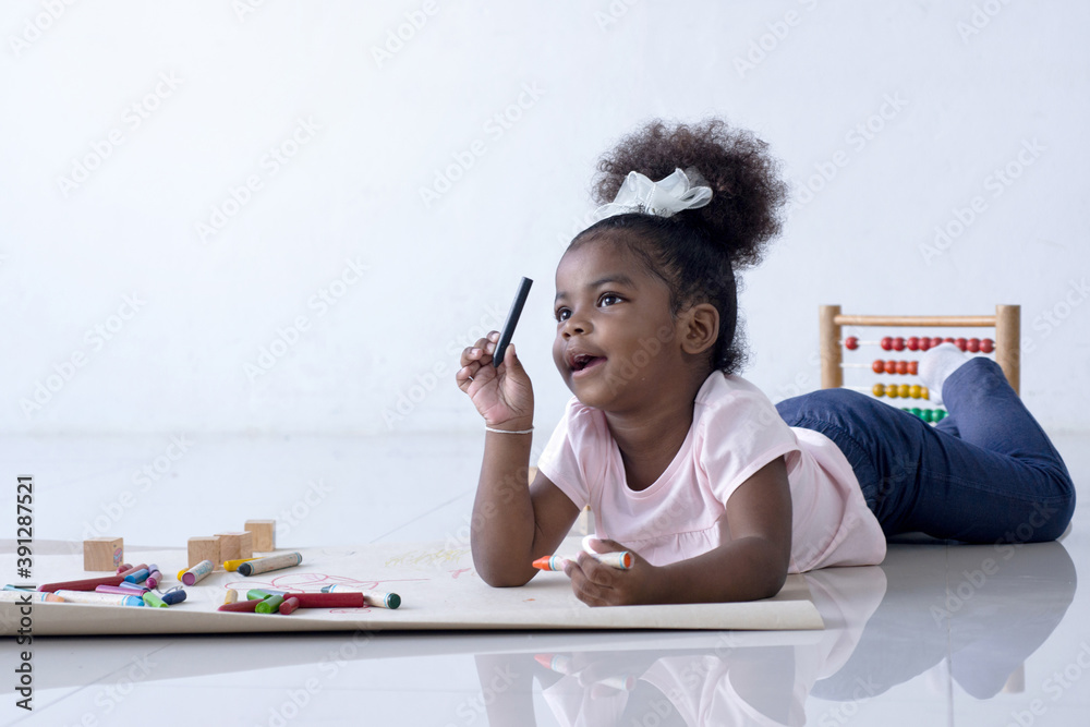 Dark-skinned child girl was lying on the floor and smiling at someone, against building background