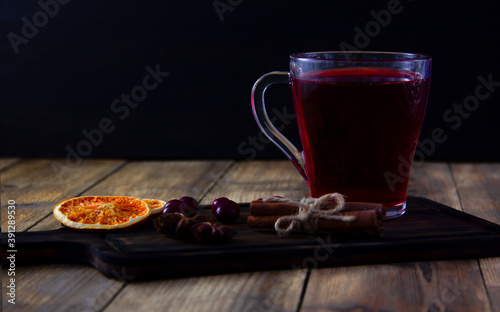 Drink from fresh cranberries in a glass on a dark wooden cutting board. Orange slices, cinnamon and anise on a wooden table.