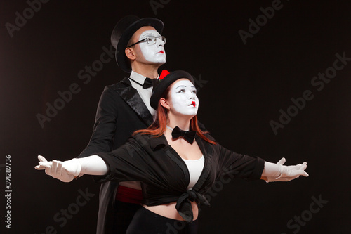 Portrait of two mime artists performing, isolated on black background. Man is standing behind the woman holding her hands.
