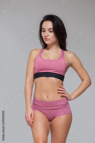 Attractive young brunette woman in pink sportswear is posing isolated on grey background © satyrenko