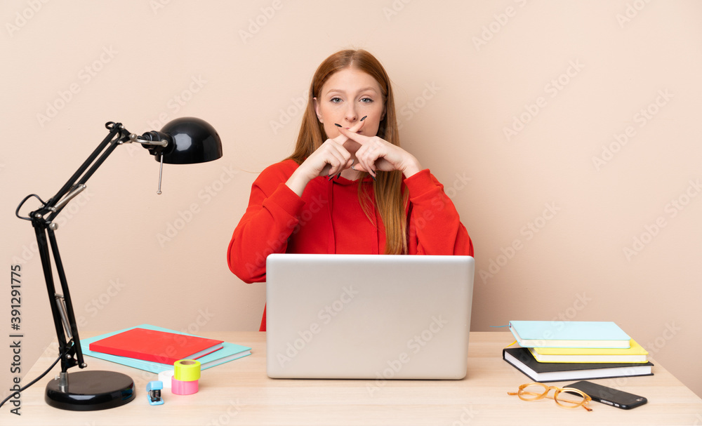 Young student woman in a workplace with a laptop showing a sign of silence gesture Young student woman in a workplace with a laptop showing a sign of silence gesture
