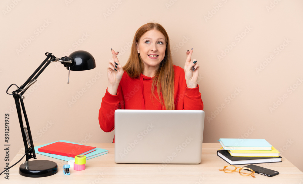 Young student woman in a workplace with a laptop with fingers crossing and wishing the best Young student woman in a workplace with a laptop with fingers crossing and wishing the best