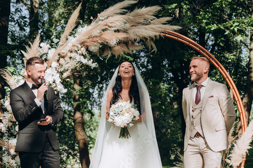 The host at the wedding interviews the bride and groom. Newlyweds on the background of a floral arch.
