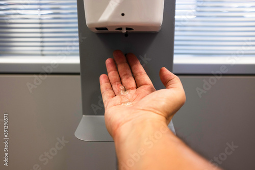 Male hand using automatic alcohol dispenser for cleaning hands in the office or hospital to sanitize virus and bacteria - Infection prevention concept - Main focus on the palm of the hand