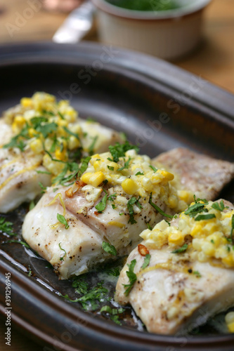 Gourmet cooked fish with corn and herbs on top on plate
