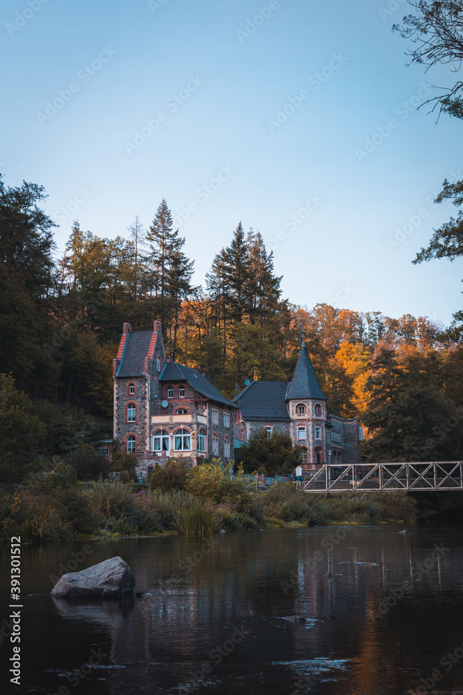 Fototapeta premium Traditionelle deutsches Haus am Ufer eines Flusses, während des Herbst im Harz (Hochformat)