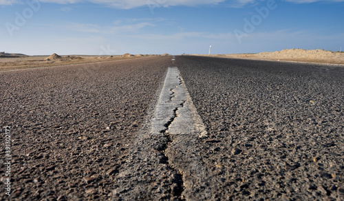 low angle shot of an asphalt road into the desert with blue sky and sandy dunes