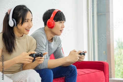 Couples play games and listen to sound through bluetooth headphones and sitting on sofa at the weekend.