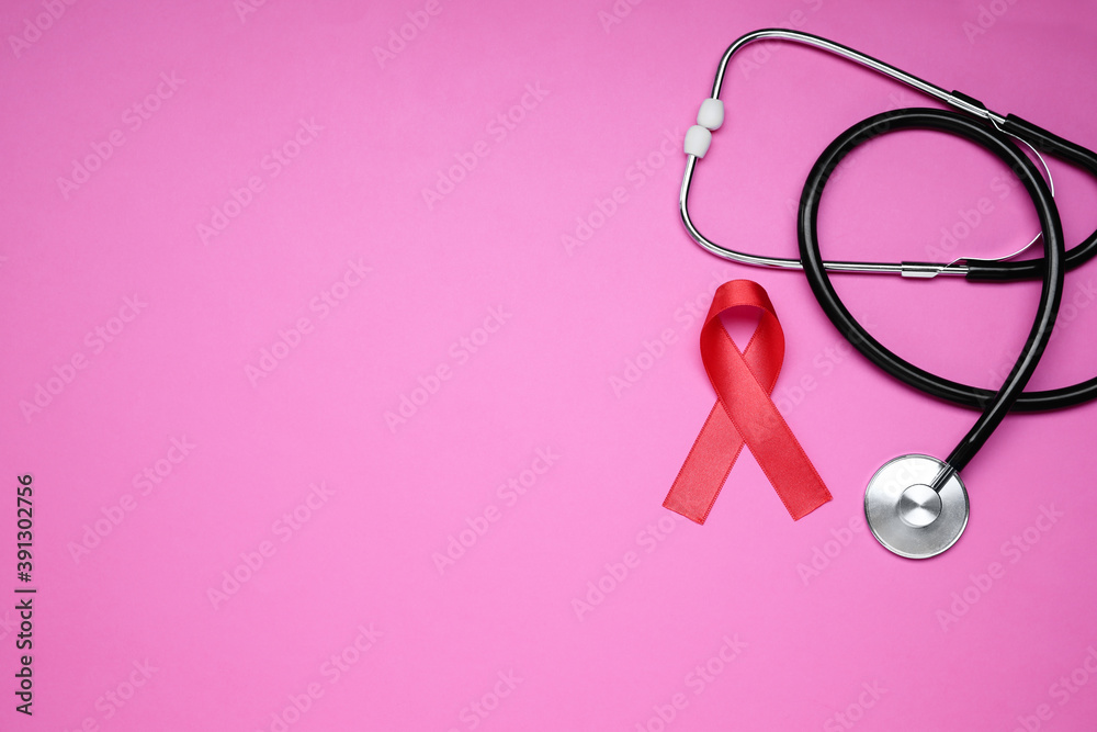 Red ribbon and stethoscope on pink background, flat lay with space for text. AIDS disease awareness Red ribbon and stethoscope on pink background, flat lay with space for text. AIDS disease awareness