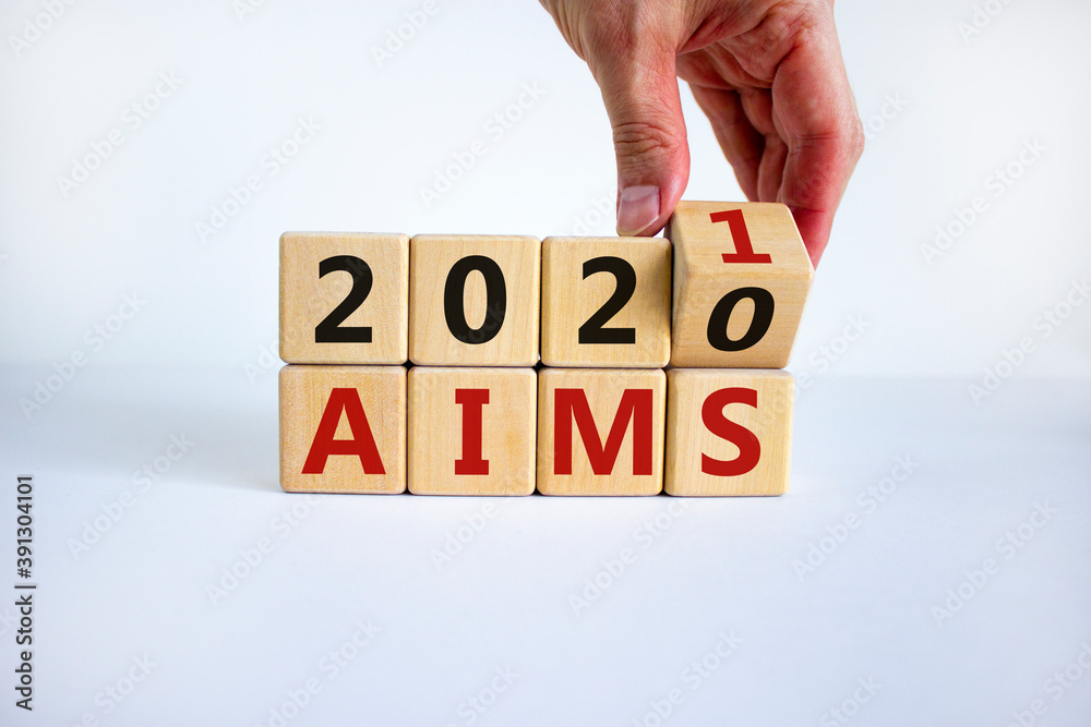 Business concept of planning 2021. Male hand flips a wooden cube and changes the inscription 'Aims 2020' to 'Aims 2021'. Beautiful white background, copy space. Business concept of planning 2021. Male hand flips a wooden cube and changes the inscription 'Aims 2020' to 'Aims 2021'. Beautiful white background, copy space.