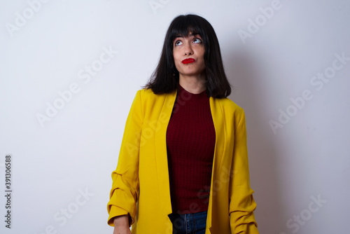 Caucasian woman standing against white background wearing yellow blazer, looks pensively aside, plans actions after university, imagines what to do Thinks over about new project. © Jihan