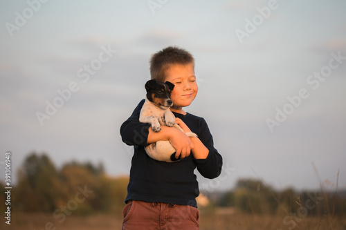 Cute boy playing with his dog in the meadow. Little puppy jack russel terrier on the walk with owner.