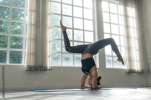 Asian woman practicing yoga standing in handstand (Adho Mukha Vrksasana) exercise on mat at fitness studio. female balancing body. flexibility workout healthy and wellness lifestyle concept