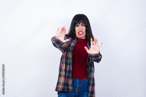 Dissatisfied Beautiful young Caucasian woman standing against white background frowns face, has disgusting expression, shows tongue, expresses non compliance, irritated with somebody. photo