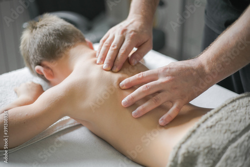 Professional Physiotherapist is treating a kid in clinic. Boy toddler relaxes from a therapeutic massage.