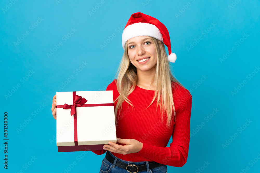 Woman with christmas hat holding a present isolated on blue background smiling a lot Woman with christmas hat holding a present isolated on blue background smiling a lot