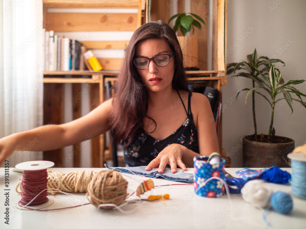 A Young Attractive Hispanic Woman in Black Dress is on a Table Making Crafts with Cloth and Threads A Young Attractive Hispanic Woman in Black Dress is on a Table Making Crafts with Cloth and Threads