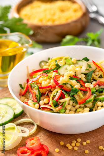 Vegetable salad with ptitim close-up. Salad made from toasted pasta ptitim (petit plomb or Israeli couscous), cucumbers, peppers, onions, and parsley. Vegan food. Mediterranean and Israeli cuisine.