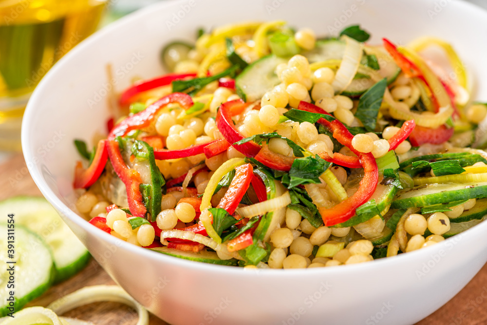 Vegetable salad with ptitim close-up. Salad made from toasted pasta ptitim (petit plomb or Israeli couscous), cucumbers, peppers, onions, and parsley. Vegan food. Mediterranean and Israeli cuisine. Vegetable salad with ptitim close-up. Salad made from toasted pasta ptitim (petit plomb or Israeli couscous), cucumbers, peppers, onions, and parsley. Vegan food. Mediterranean and Israeli cuisine.