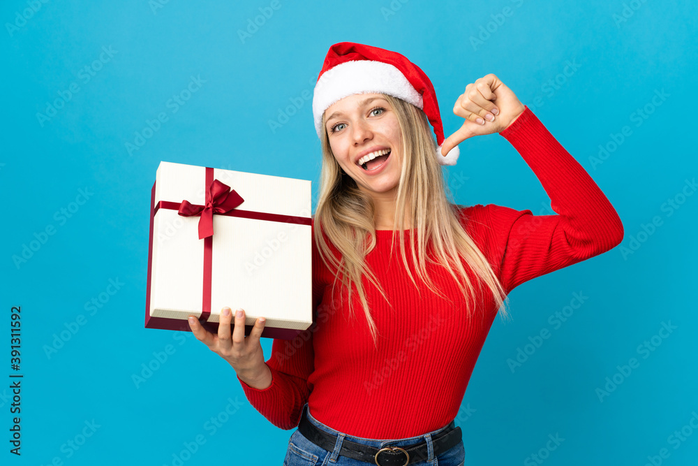 Woman with christmas hat holding a present isolated on blue background proud and self-satisfied Woman with christmas hat holding a present isolated on blue background proud and self-satisfied