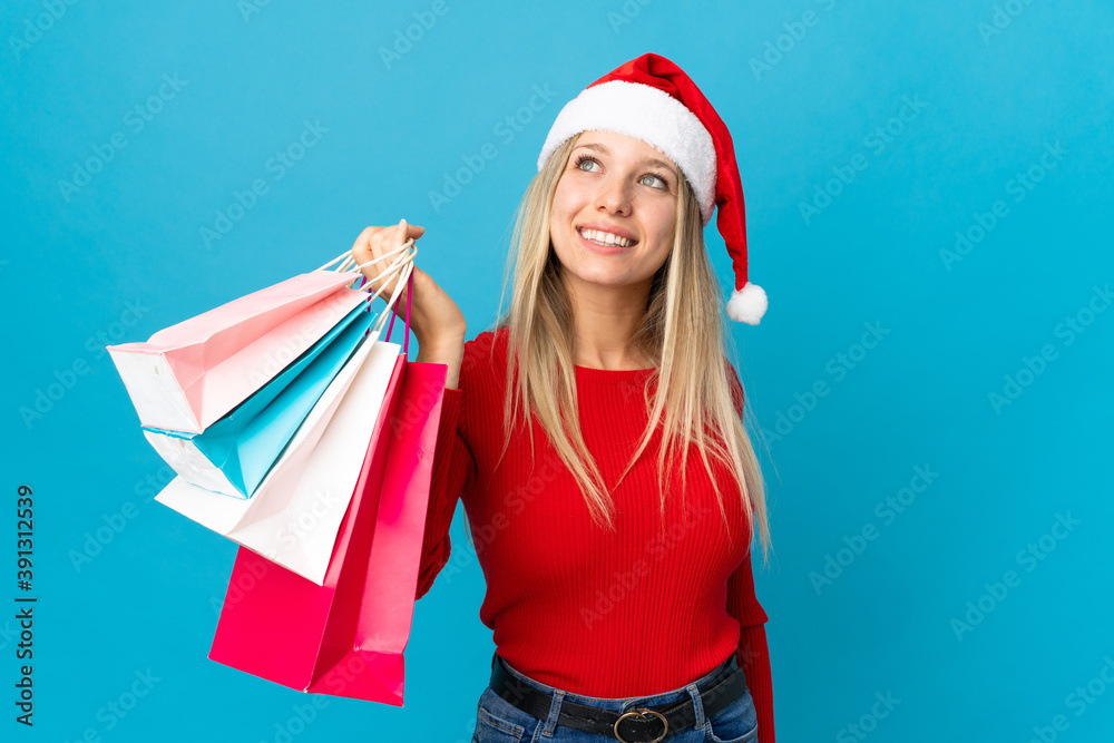 Obraz premium Woman with christmas hat going to buy something isolated on blue background looking up while smiling