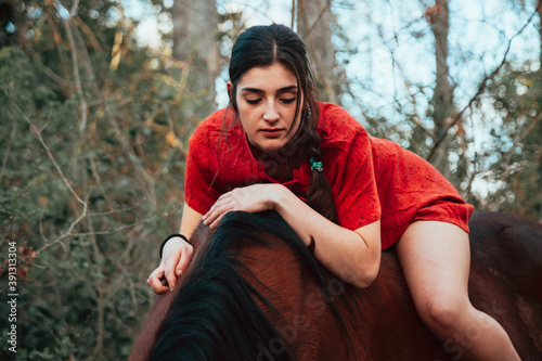 Beautiful young woman hugging brown horse and wearing dress photo