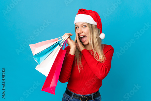 Woman with christmas hat going to buy something isolated on blue background whispering something