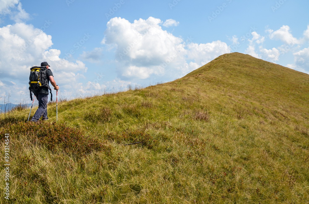Hiker with backpack walking on trail uphill to mountain top in Carpathian mountains, Ukraine