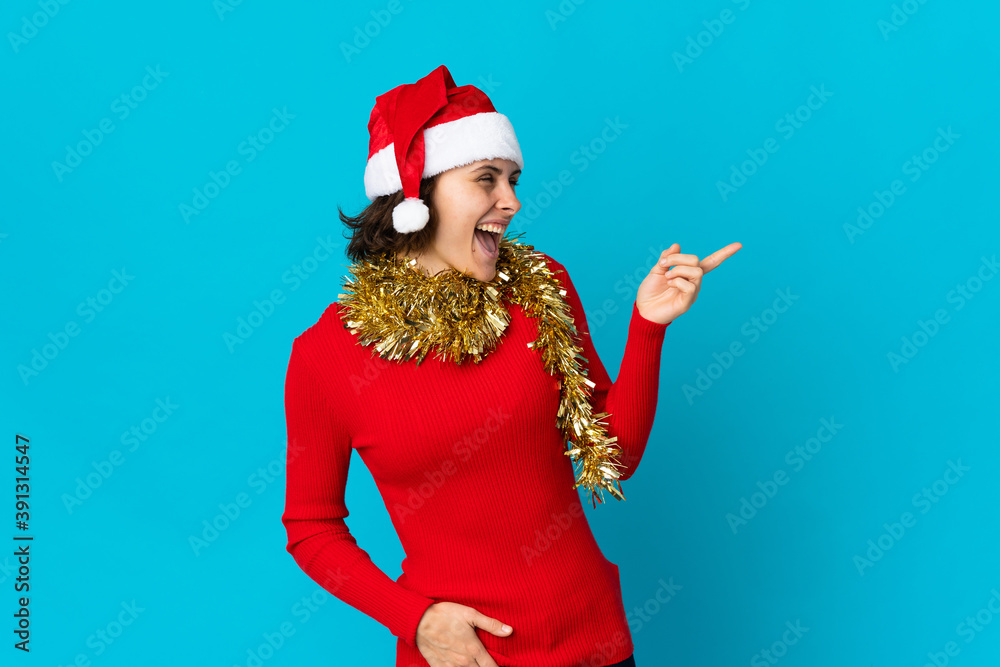 English girl with christmas hat isolated on blue background pointing finger to the side and presenting a product English girl with christmas hat isolated on blue background pointing finger to the side and presenting a product