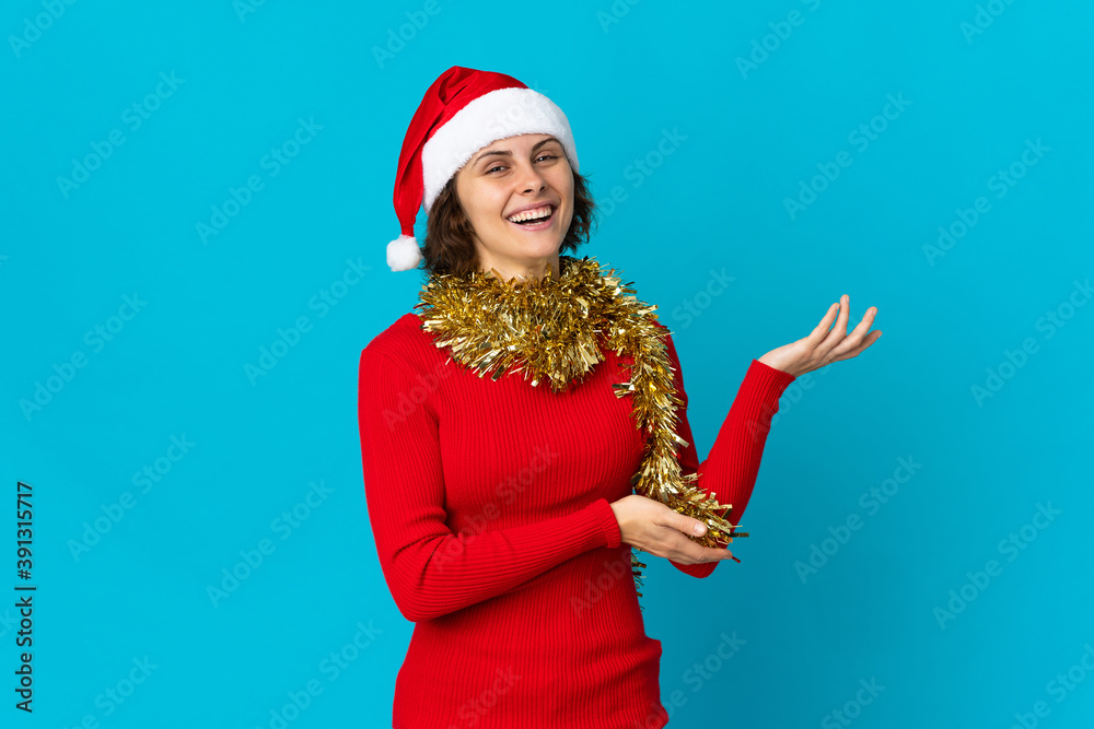English girl with christmas hat isolated on blue background extending hands to the side for inviting to come English girl with christmas hat isolated on blue background extending hands to the side for inviting to come