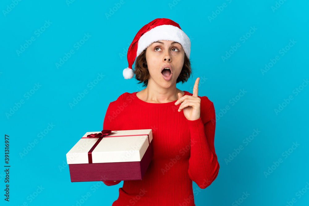 English girl with christmas hat holding a present isolated on blue background thinking an idea pointing the finger up English girl with christmas hat holding a present isolated on blue background thinking an idea pointing the finger up