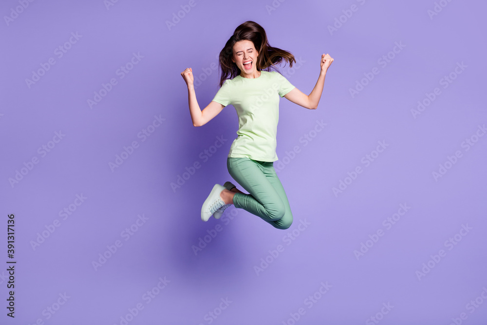 Photo portrait full body view of cheerful girl celebrating victory with raised fists jumping up isolated on vivid violet colored background Photo portrait full body view of cheerful girl celebrating victory with raised fists jumping up isolated on vivid violet colored background