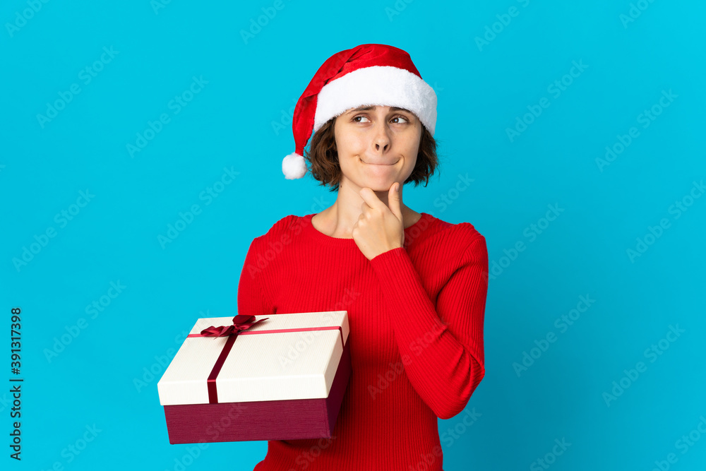 English girl with christmas hat holding a present isolated on blue background having doubts and thinking English girl with christmas hat holding a present isolated on blue background having doubts and thinking