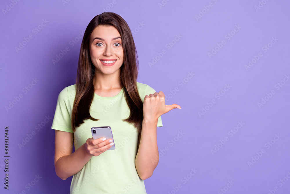 Photo portrait of happy girl holding smartphone pointing at empty space smiling isolated on vivid violet color background Photo portrait of happy girl holding smartphone pointing at empty space smiling isolated on vivid violet color background