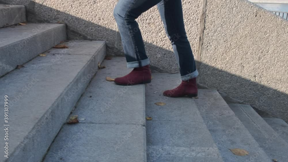 Female legs in burgundy boots and blue jeans climb the stone stairs on a sunny autumn day. No people Female legs in burgundy boots and blue jeans climb the stone stairs on a sunny autumn day. No people