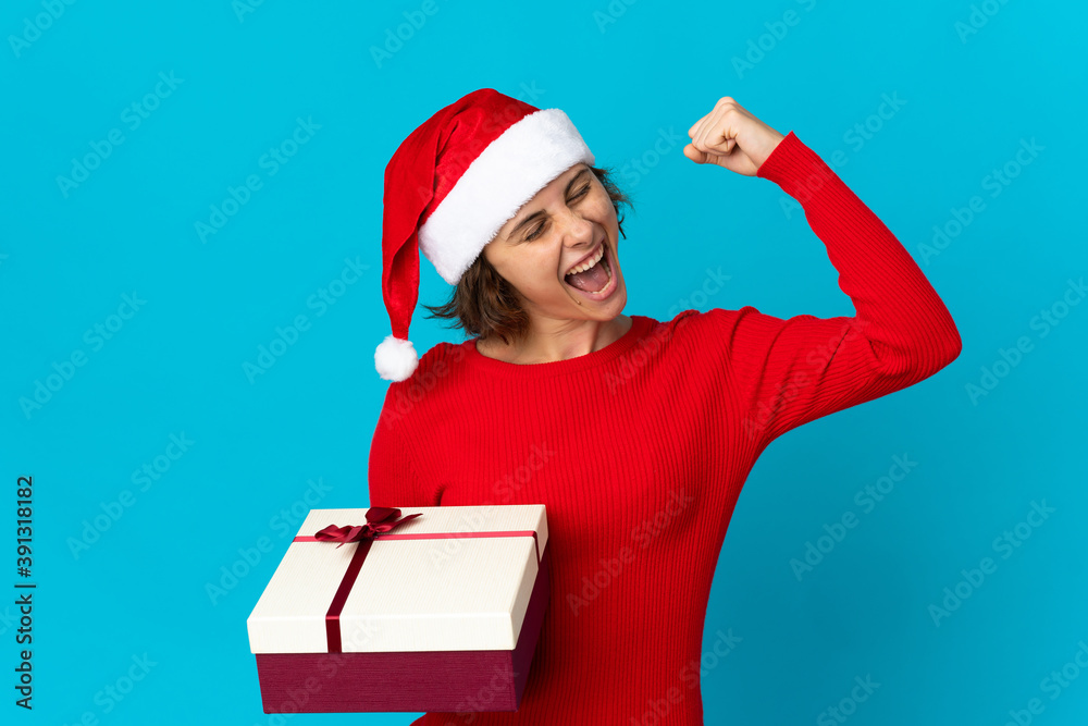 English girl with christmas hat holding a present isolated on blue background celebrating a victory English girl with christmas hat holding a present isolated on blue background celebrating a victory