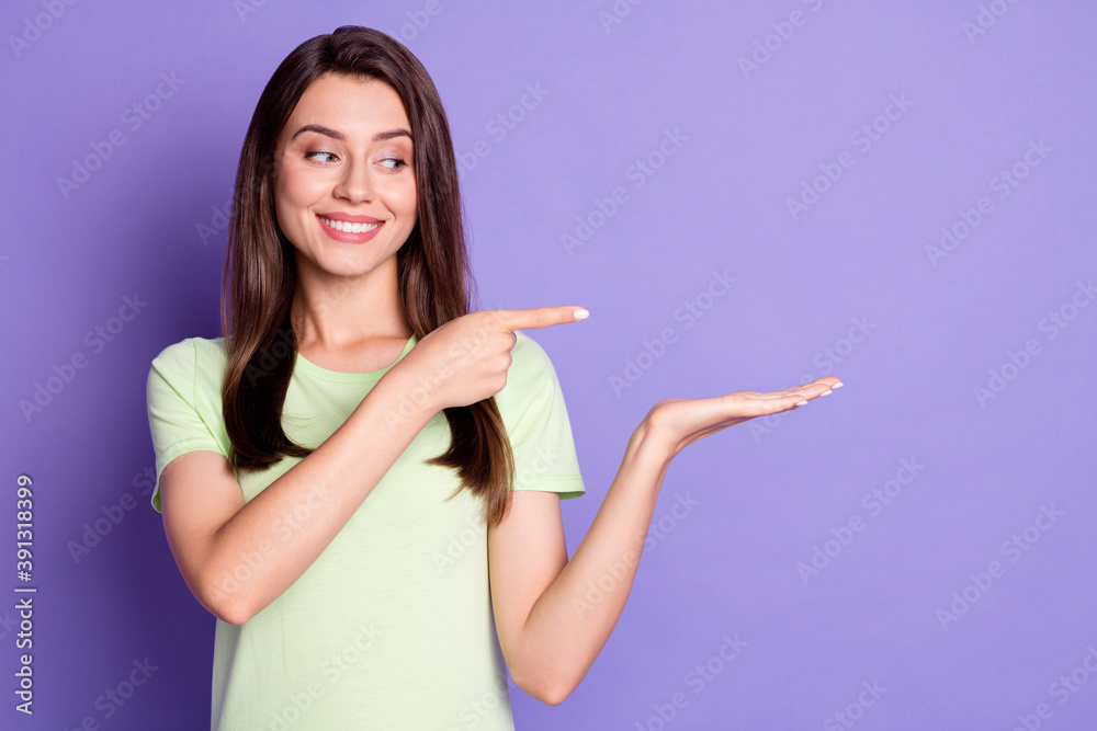 Photo portrait of curious girl pointing demonstrating looking at blank space on hand smiling isolated on vibrant purple color background